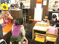 東京都中央区日本橋にある老舗百貨店の子供用品フロアでお絵かきをしているお子様の前でバルーンアートを作るピエロ(クラウン)に釘付けになっている女の子 お絵かきコーナーにいるお子様の前でバルーンを作るピエロ(クラウン)