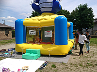 長野県安曇野市の社会福祉協議会が開催した夏祭りでキッズコーナーとして設置したエア遊具(ふわふわ)で遊ぶお子様と外から中の様子を伺う保護者の方々 青い恐竜が上についたエア遊具(ふわふわ)の中で遊ぶお子様を見守る保護者の方々