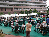 千葉県柏市にあるマンションの夏祭りで提供された食事やドリンクを手に座って休憩したり、ダンスなどの出し物を見ている住民の方々 マンション夏祭りの飲食・休憩スペース